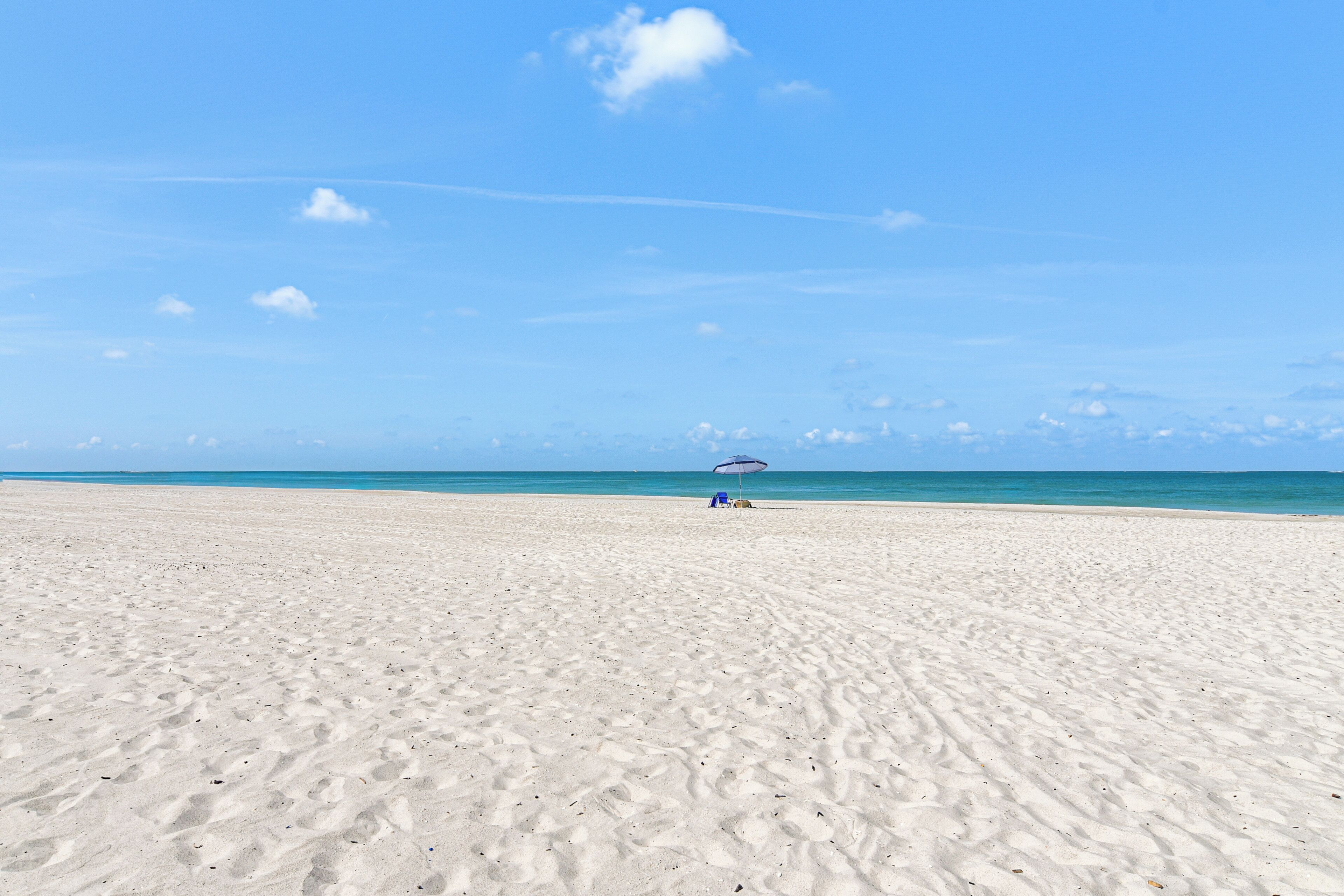 A wide sandy beach with a clear blue sky and a distant view of the ocean.