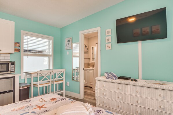 A room with teal walls, a white dresser, a bed with a starfish-themed bedspread, a microwave, and a small kitchen area.