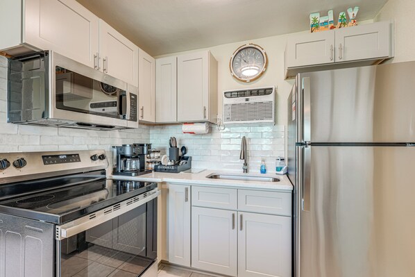 A kitchen with white cabinets, a stainless steel refrigerator, a microwave, an oven, and a sink. - Beachfront Condo: Redington Shores Retreat! (Redington Shores)