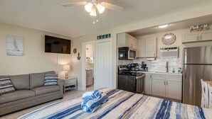 A bedroom with a bed, a sofa, a kitchenette with a refrigerator, microwave, and stove, and a ceiling fan. - Beachfront Condo: Redington Shores Retreat! (Redington Shores)