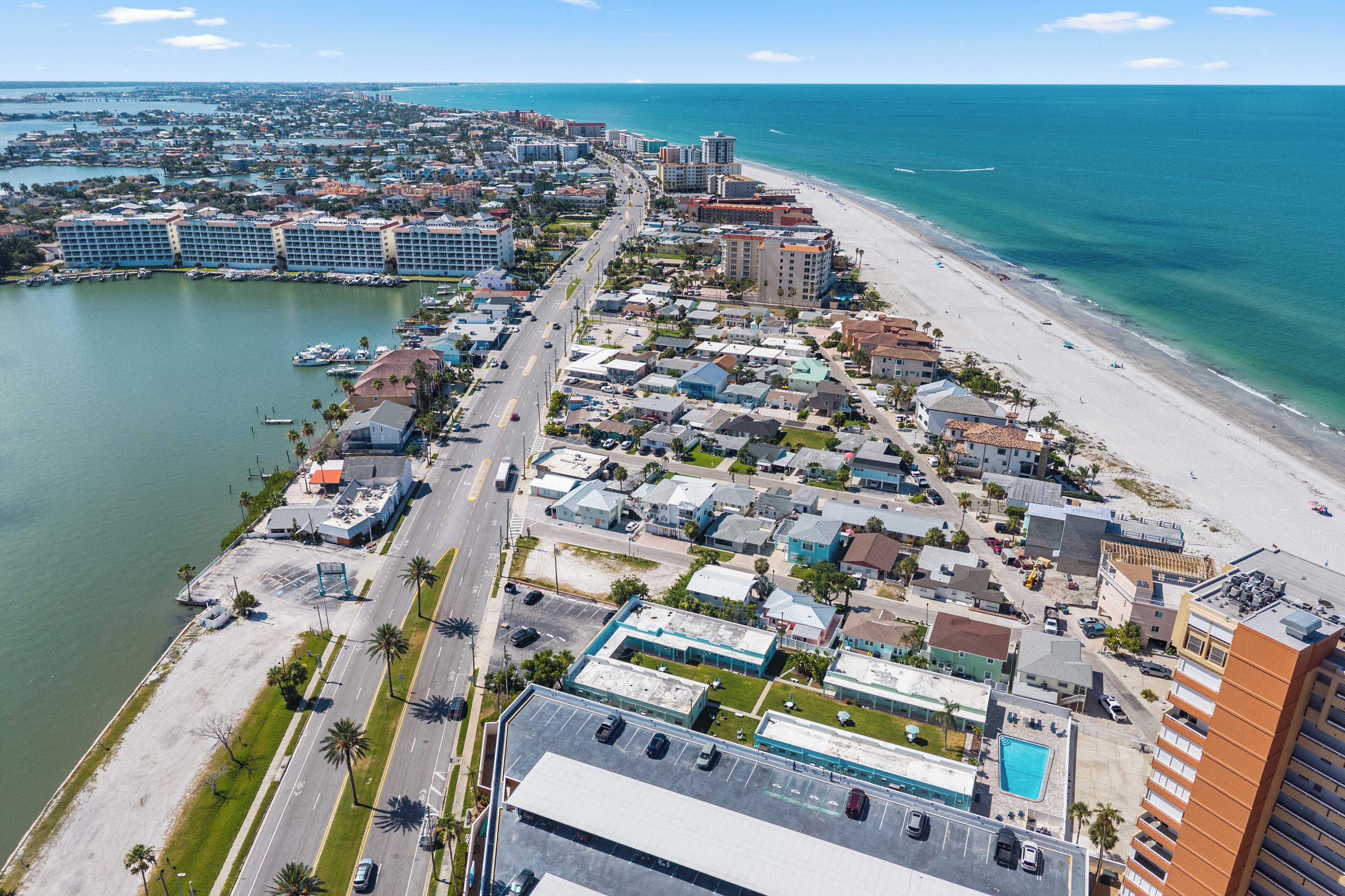 An aerial view of a coastal city with a marina, beachfront, and various buildings.