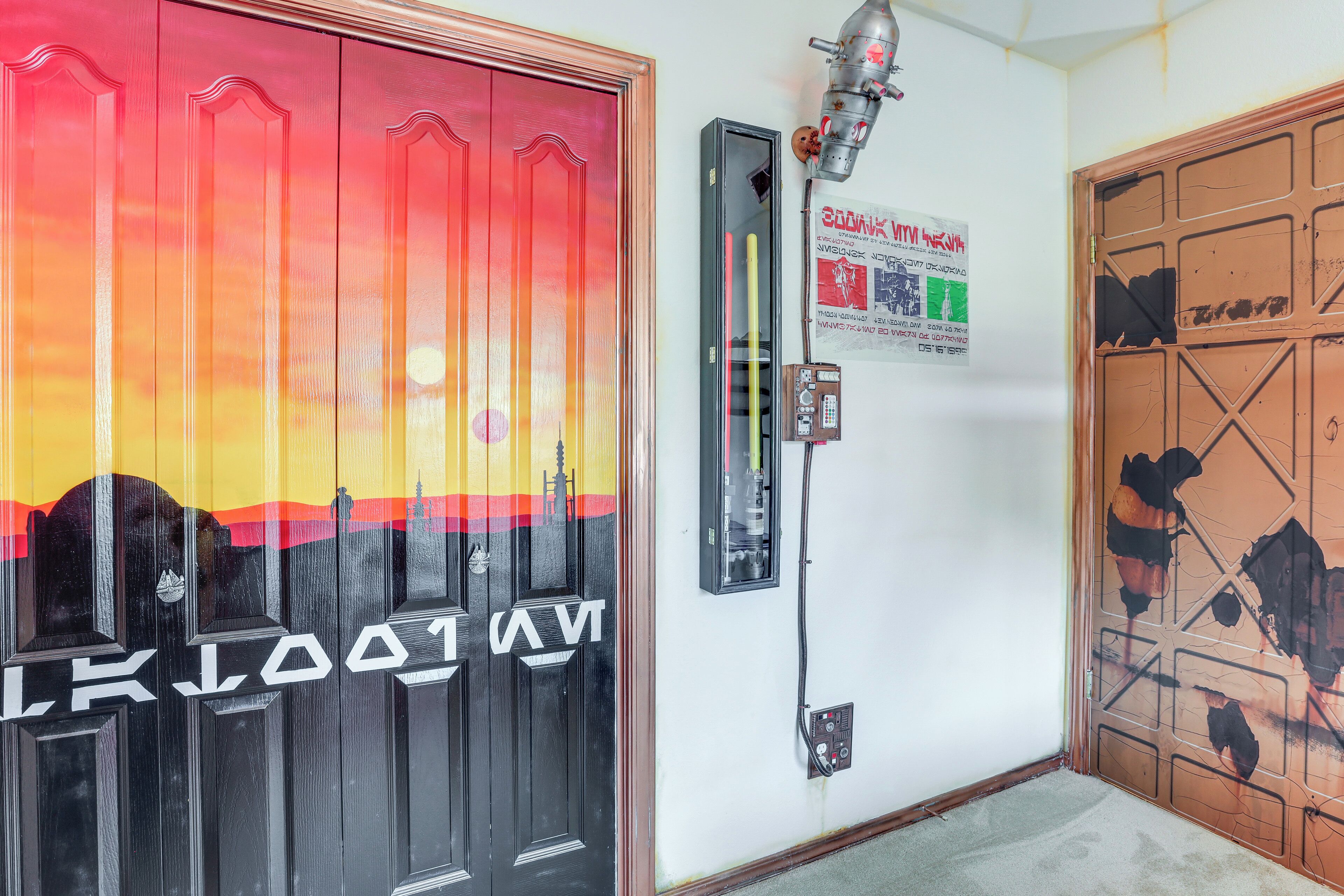 A hallway with a black door featuring a sunset mural, a security intercom, and a poster on the wall.