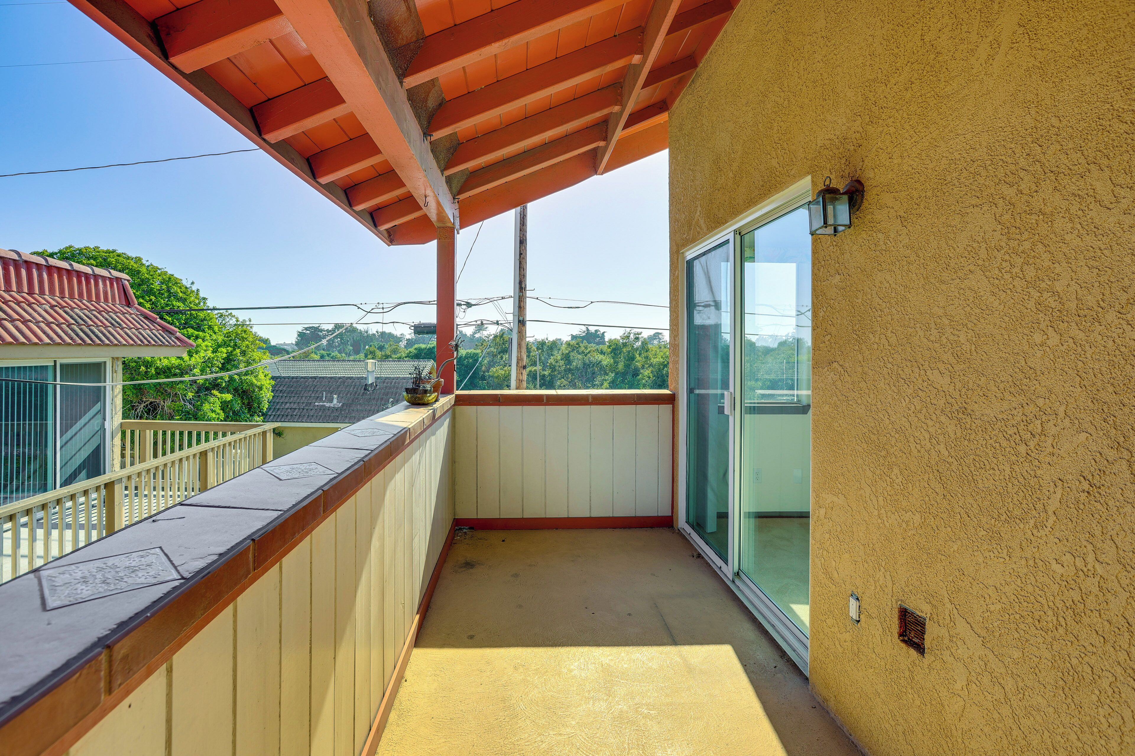 Un balcone con ringhiera in legno, una porta in vetro e vista su spazi verdi ed edifici sullo sfondo.