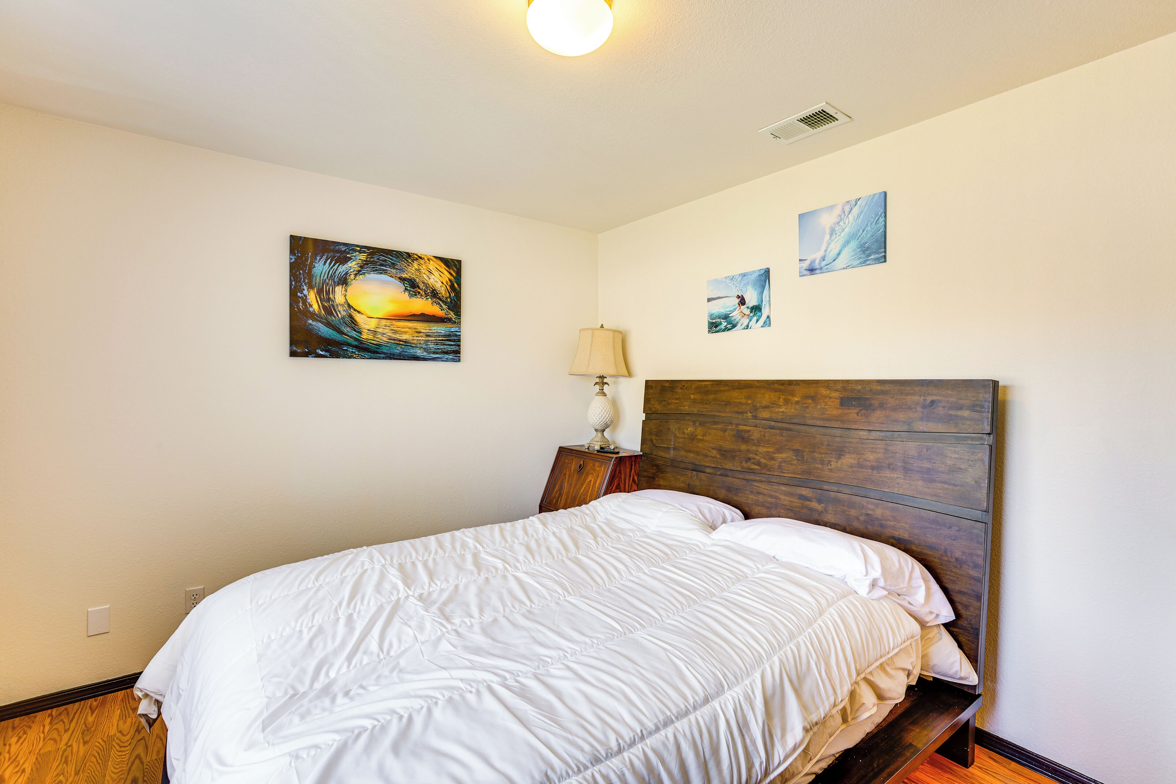 Un lit bien fait, avec une tête de lit en bois, une lampe de chevet et trois tableaux accrochés au mur.