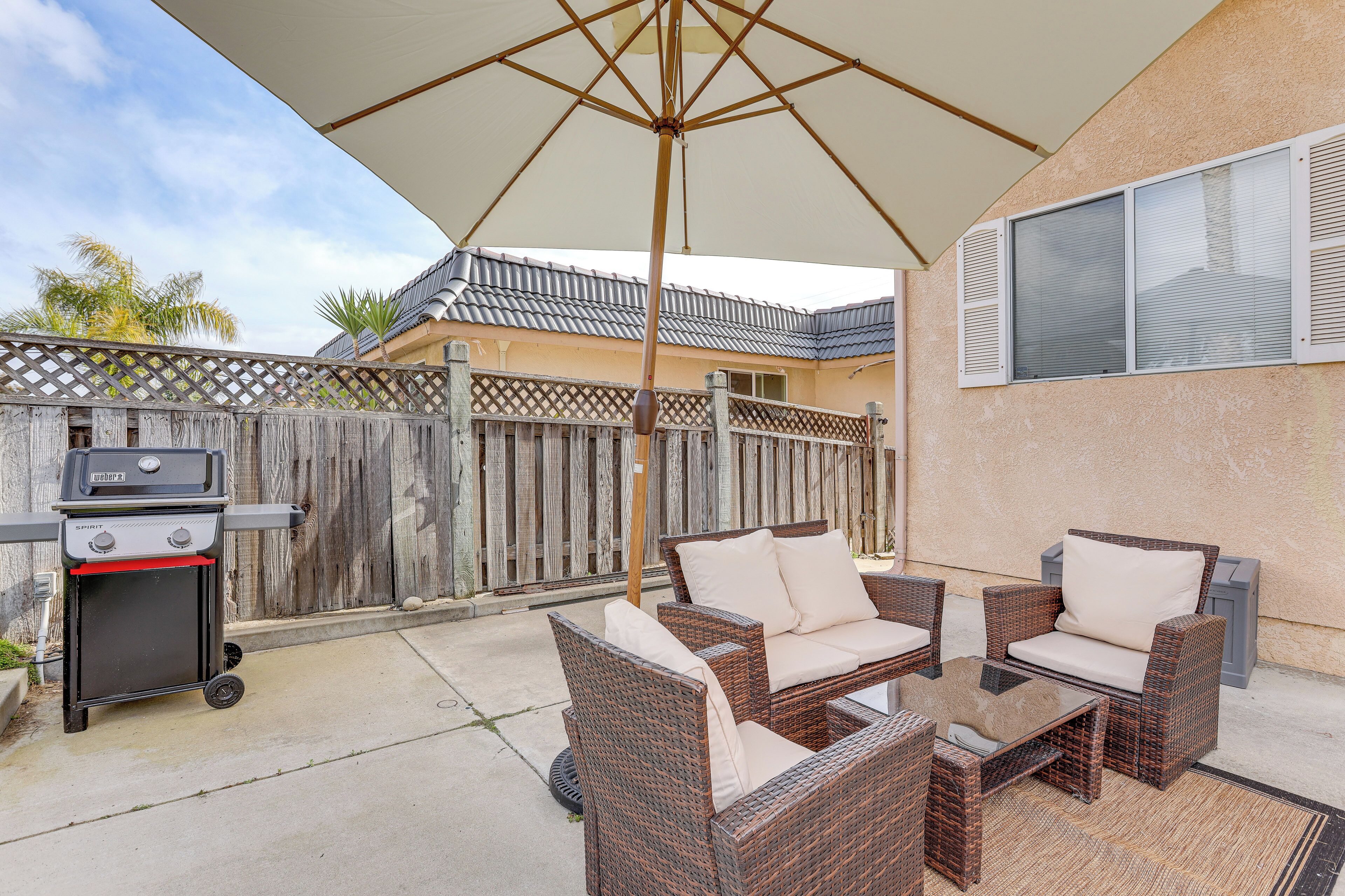 An outdoor patio with wicker furniture, a grill, and a large umbrella.
