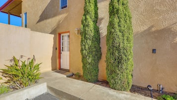 Stucco exterior with a simple, functional design, featuring a wooden door and lush greenery.