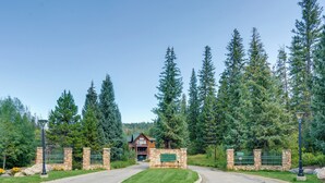 A lodge entrance with a stone wall, a green fence, and tall trees in the background. - Gem in Old Town Winter Park: Walk to Ski Lifts! (Winter Park)