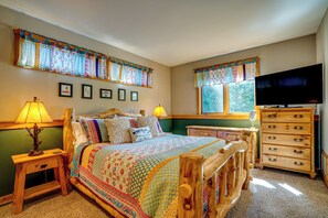 Un dormitorio con cama de madera, cómoda, televisor y ventana con cortinas.