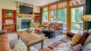 A cozy living room with a stone fireplace, comfortable seating, and large windows offering a view of the outdoors. - Gem in Old Town Winter Park: Walk to Ski Lifts! (Winter Park)