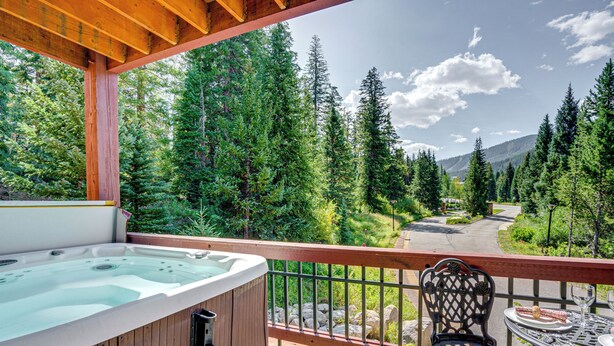 A hot tub on a wooden deck with a view of a forest and mountains. - Gem in Old Town Winter Park: Walk to Ski Lifts! (Winter Park)