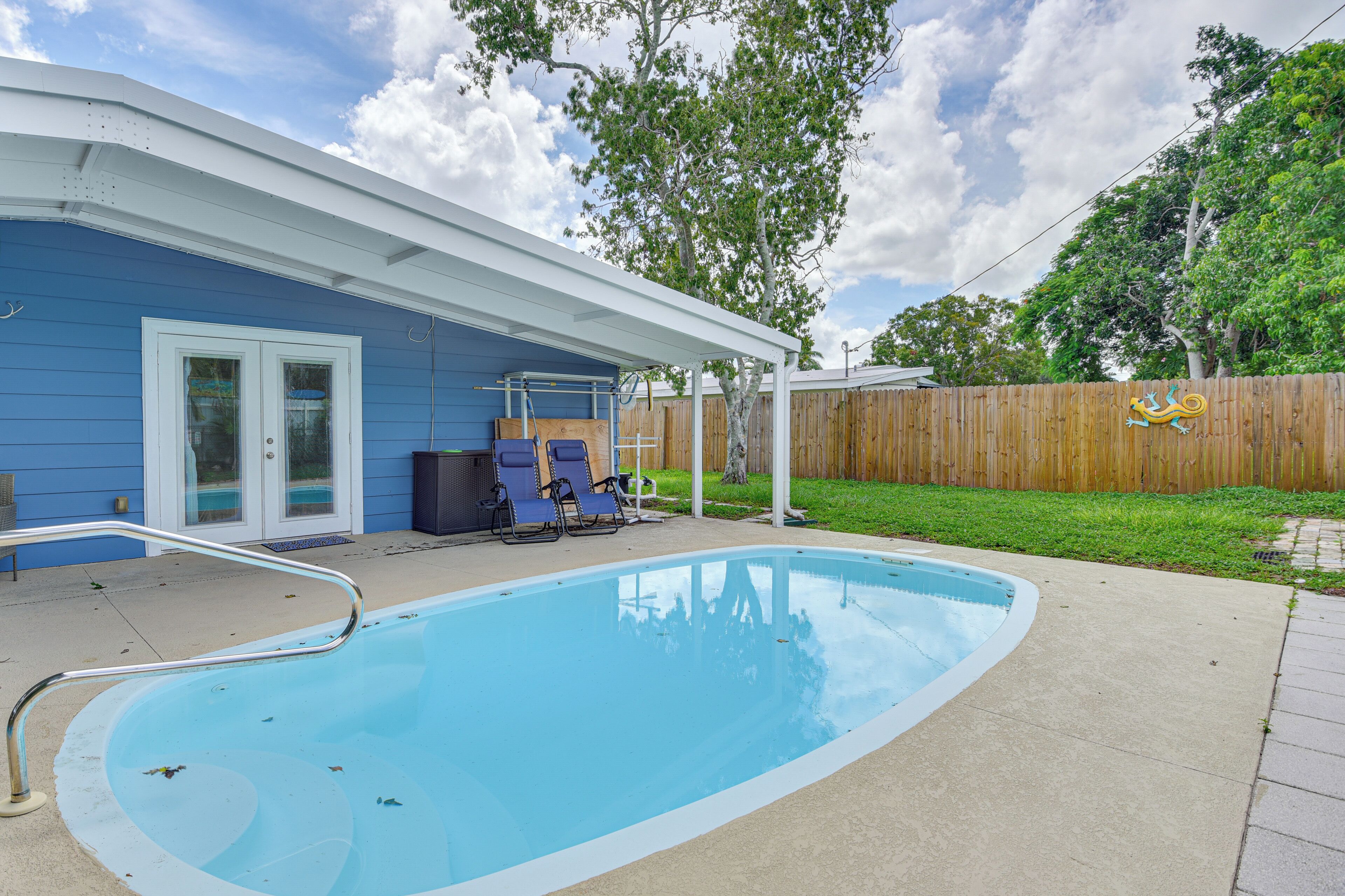 Una piscina con un deck blanco, un patio techado y una valla de madera al fondo.