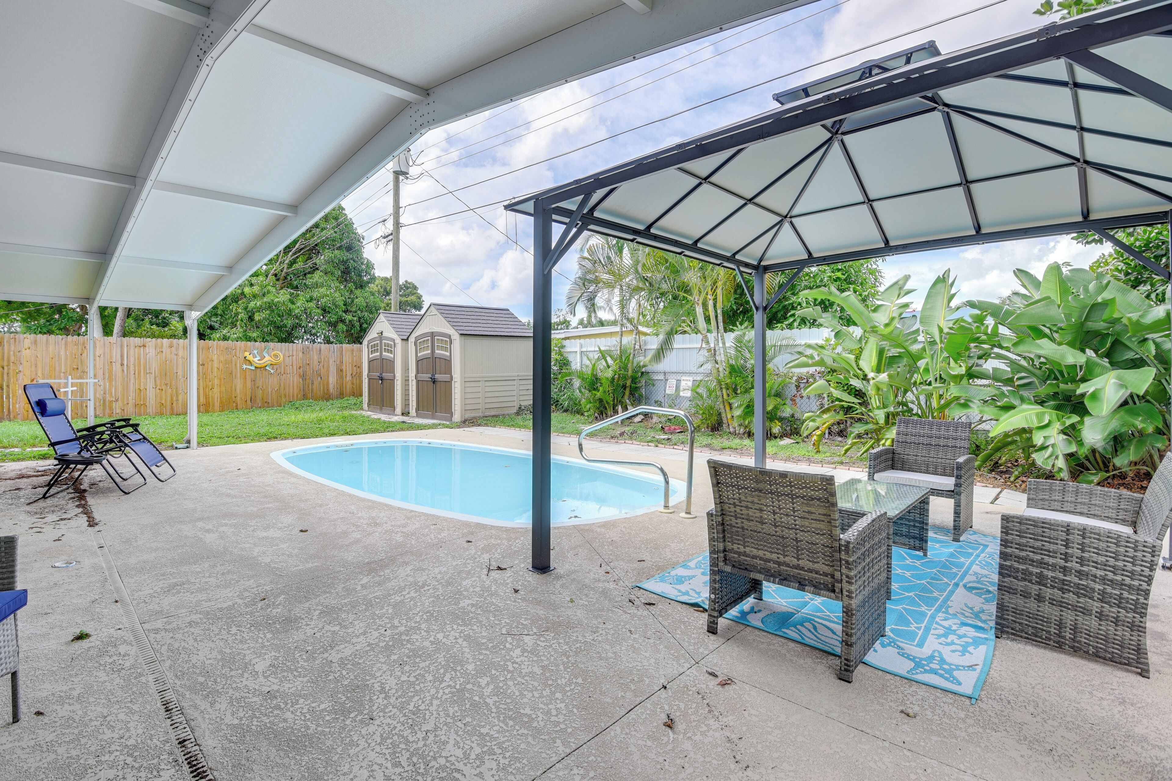 Eine überdachte Terrasse mit Pool, Gartenmöbeln und einem kleinen Schuppen im Hintergrund.