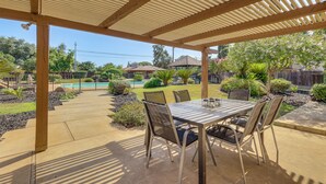 A covered patio with a table and chairs, a pool, and a garden in the background. - Spacious Home - 6 Mi to Downtown Fresno! (Fresno)