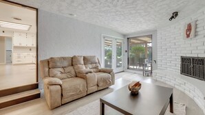 A modern living room with a beige leather sofa, a wooden coffee table, and a white brick fireplace. - Spacious Home - 6 Mi to Downtown Fresno! (Fresno)