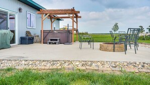 En udendørs patio med pergola, bålsted og siddepladser.