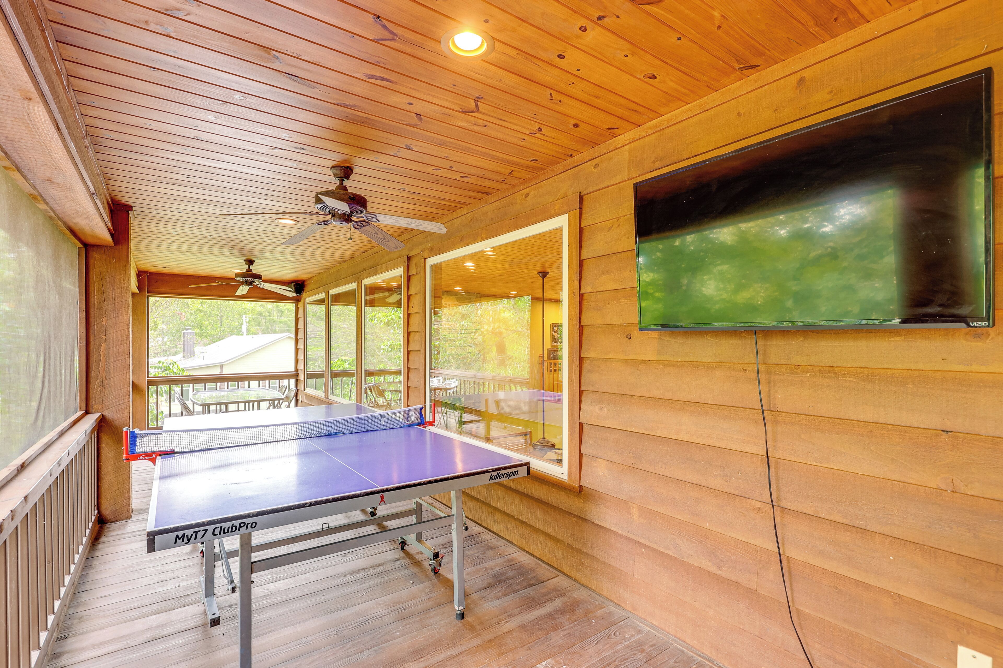 A ping pong table in a wooden room with a ceiling fan and a large window.