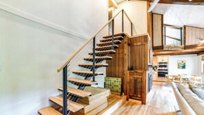 A modern kitchen with wooden cabinets, a dining area with a table and chairs, and a staircase with wooden steps and metal railings.