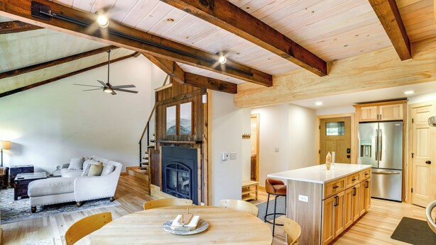 A spacious living area with a wooden ceiling, a sofa, a dining table with chairs, and a kitchen with wooden cabinets and appliances.
