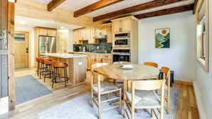 A modern kitchen with wooden cabinets, a stainless steel refrigerator, and a wooden dining table with chairs.