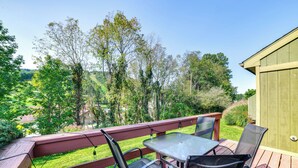 A wooden deck with a table and chairs, overlooking a green landscape with trees and a building in the background.