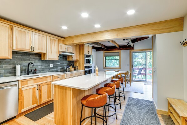 A modern kitchen with wooden cabinets, a large island with bar stools, and a view to a patio area. - Skier's Paradise: Townhome w/ Deck in Cortland! (Cortland)