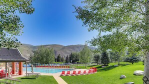 A pool area with red chairs and picnic tables, surrounded by green grass and trees, with mountains in the background. - Golf Course & Mtn Views: Avon Gem w/ Gas Grill! (Avon)
