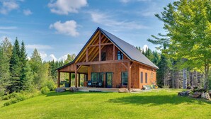 A wooden cabin with a large porch, surrounded by a lush green landscape and trees. - 'sunset House' Greensboro Forest Escape & Fire Pit (Stannard)