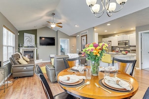 A modern living room with a fireplace, a dining area set for four, and a kitchen in the background.