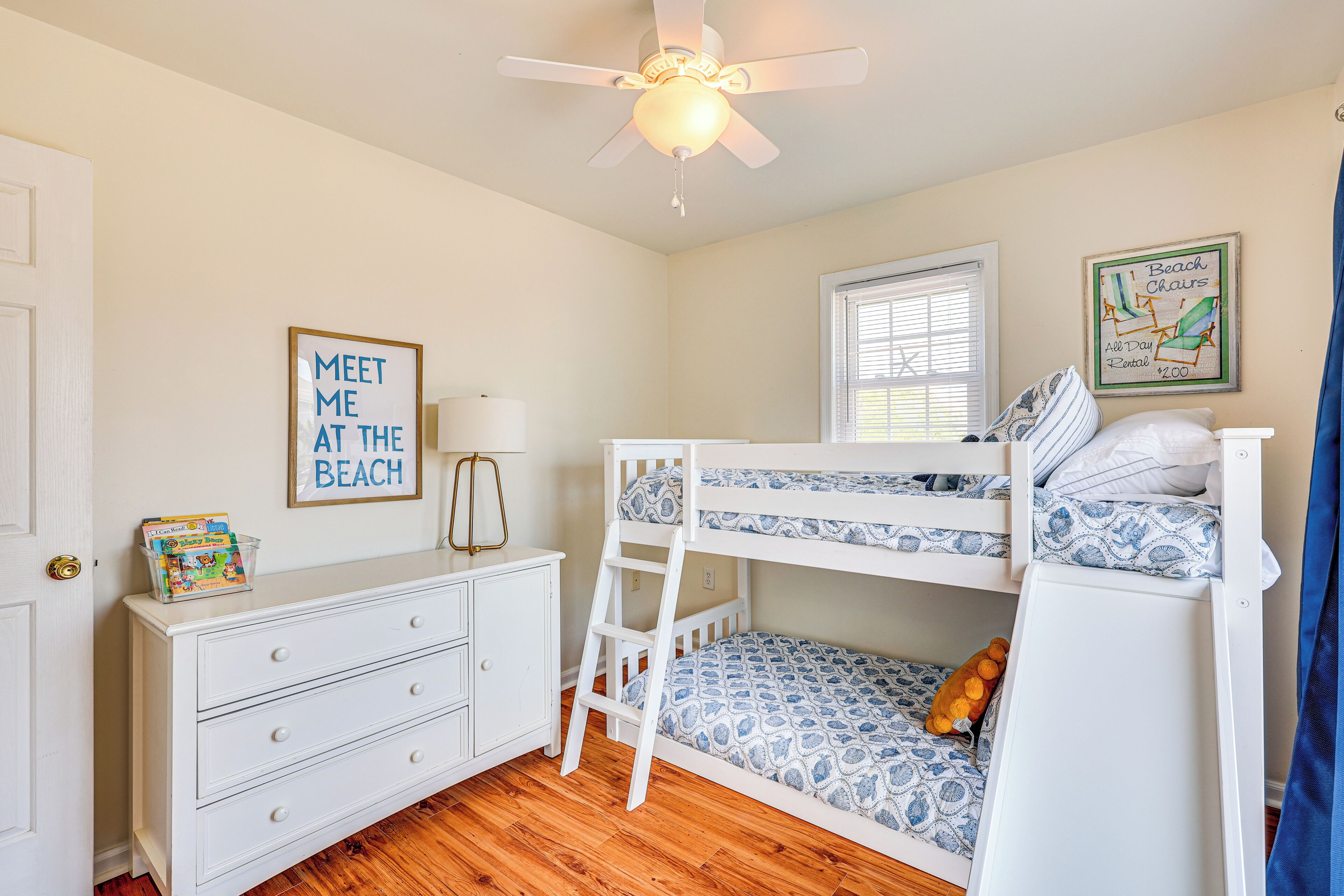 A child's bedroom with bunk beds, a dresser, a ceiling fan, and a window.