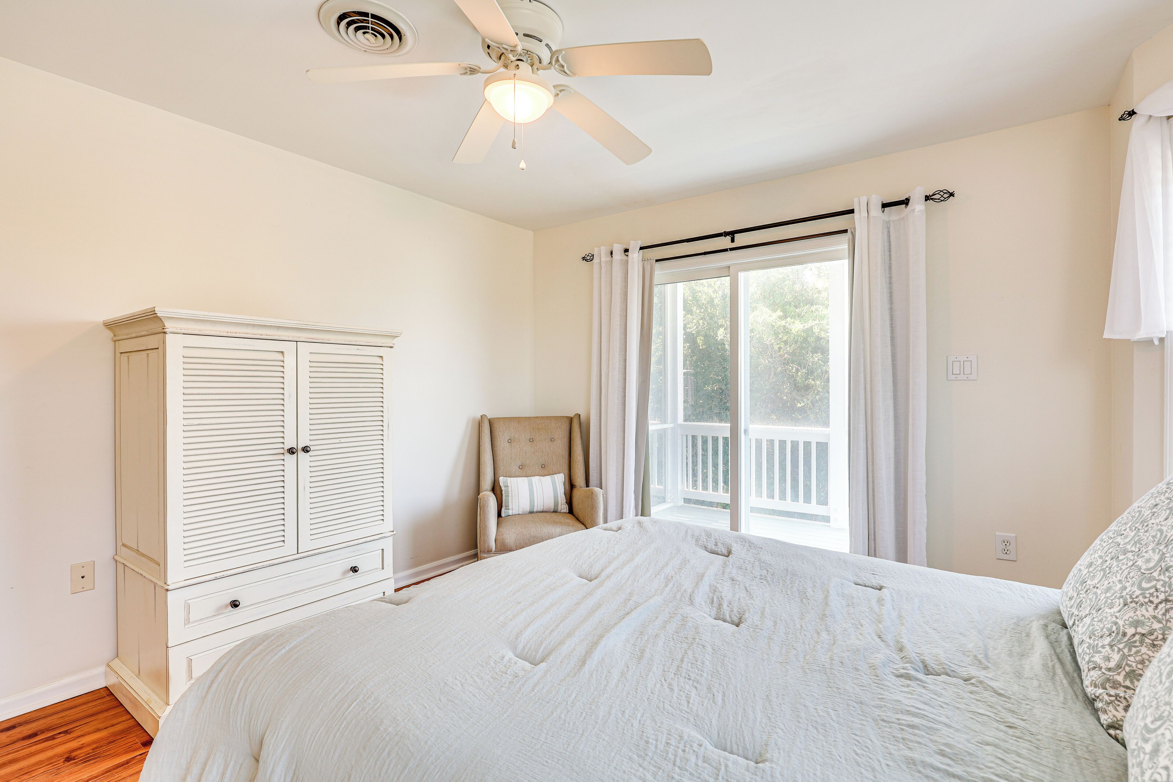 A bedroom with a large bed, a wardrobe, a chair, and a ceiling fan.