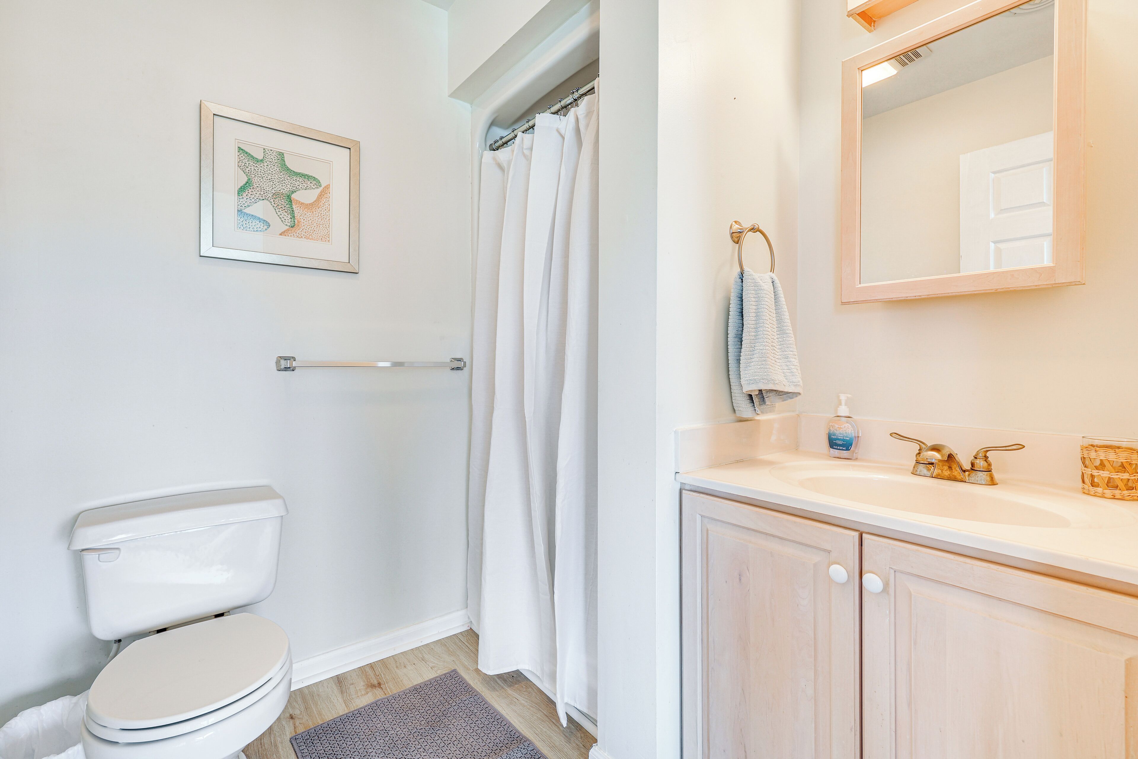 Een badkamer met een toilet, douchegordijn, wastafel met spiegel en een foto in een lijst aan de muur.