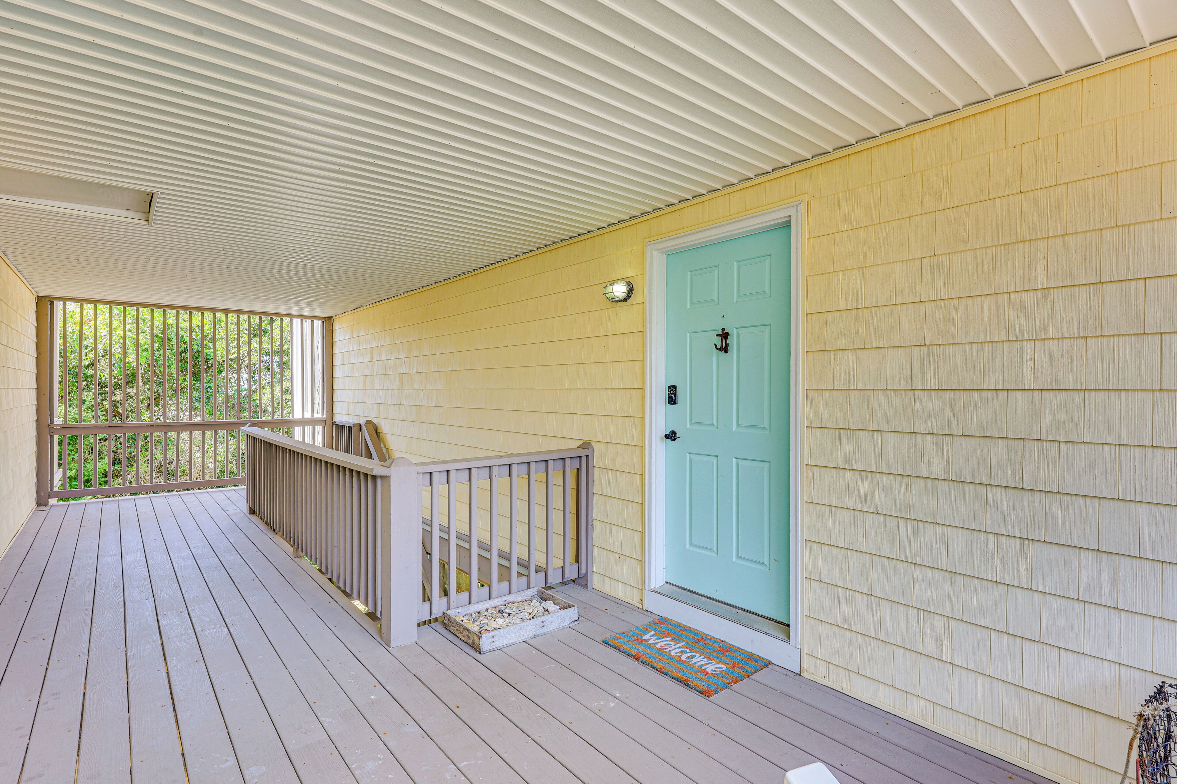 A covered porch with a wooden railing, a turquoise door, and a welcome mat.
