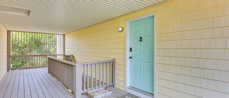 A covered porch with a wooden railing, a turquoise door, and a welcome mat.