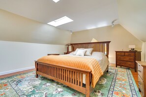 Quarto com cama de madeira, tapete estampado, mesa de cabeceira e cômoda.