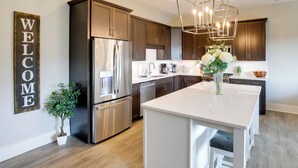 Una cocina moderna con electrodomésticos de acero inoxidable, armarios de madera oscura, una isla blanca y un letrero que dice 'WELCOME'.