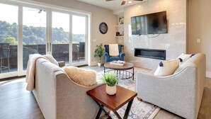 Un salón amplio con un televisor grande, asientos cómodos, un ventilador de techo y vistas a través de puertas de cristal.