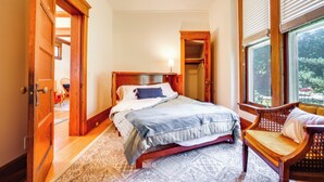 Un dormitorio con una cama de madera, una silla, una ventana con persianas y una puerta que da a otra habitación.