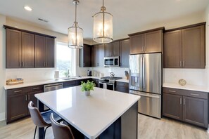 A modern kitchen with dark cabinets, stainless steel appliances, and a central island with chairs. - Pet-friendly Lynchburg Condo: Balcony w/ Views! (Lynchburg)