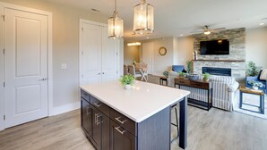 Una cocina moderna con una isla central, luces colgantes y una chimenea de piedra.