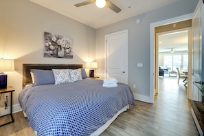 Un dormitorio con cama, lámparas de noche, un cuadro y una puerta que da a otra habitación.