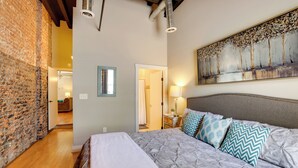 A bedroom with a large bed, a brick wall, a painting, and a wooden ceiling. - Dtwn Lynchburg Loft w/ Shared Deck: Walk to River (Lynchburg)