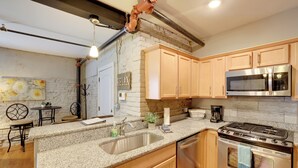 A kitchen with granite countertops, stainless steel appliances, wooden cabinets, and a brick wall. - Dtwn Lynchburg Loft w/ Shared Deck: Walk to River (Lynchburg)