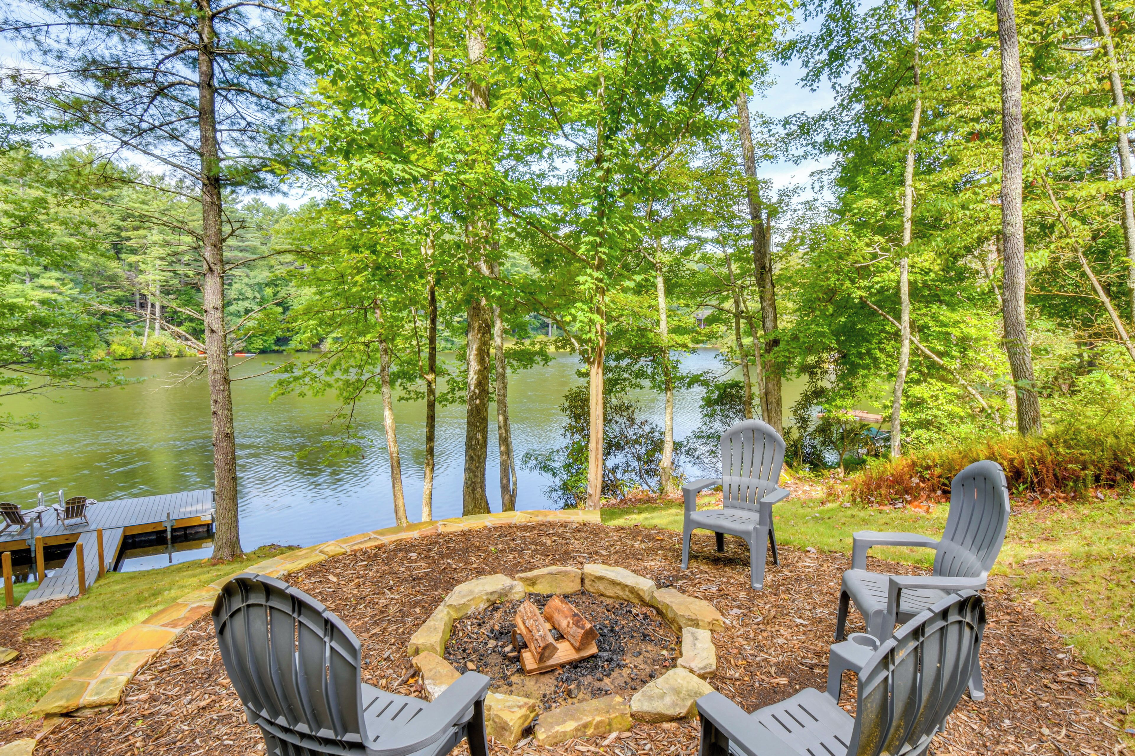 Une terrasse au bord du lac, avec des fauteuils Adirondack, un foyer et une vue sur le lac, entouré d’arbres.