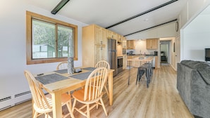 Una cocina moderna con armarios de madera, un refrigerador de acero inoxidable y un comedor con sillas y mesa de madera.