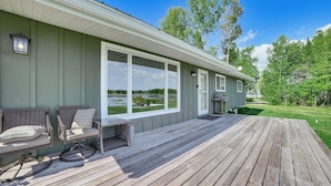 Terraza de madera con mobiliario exterior, ventanas amplias y vista a un lago.