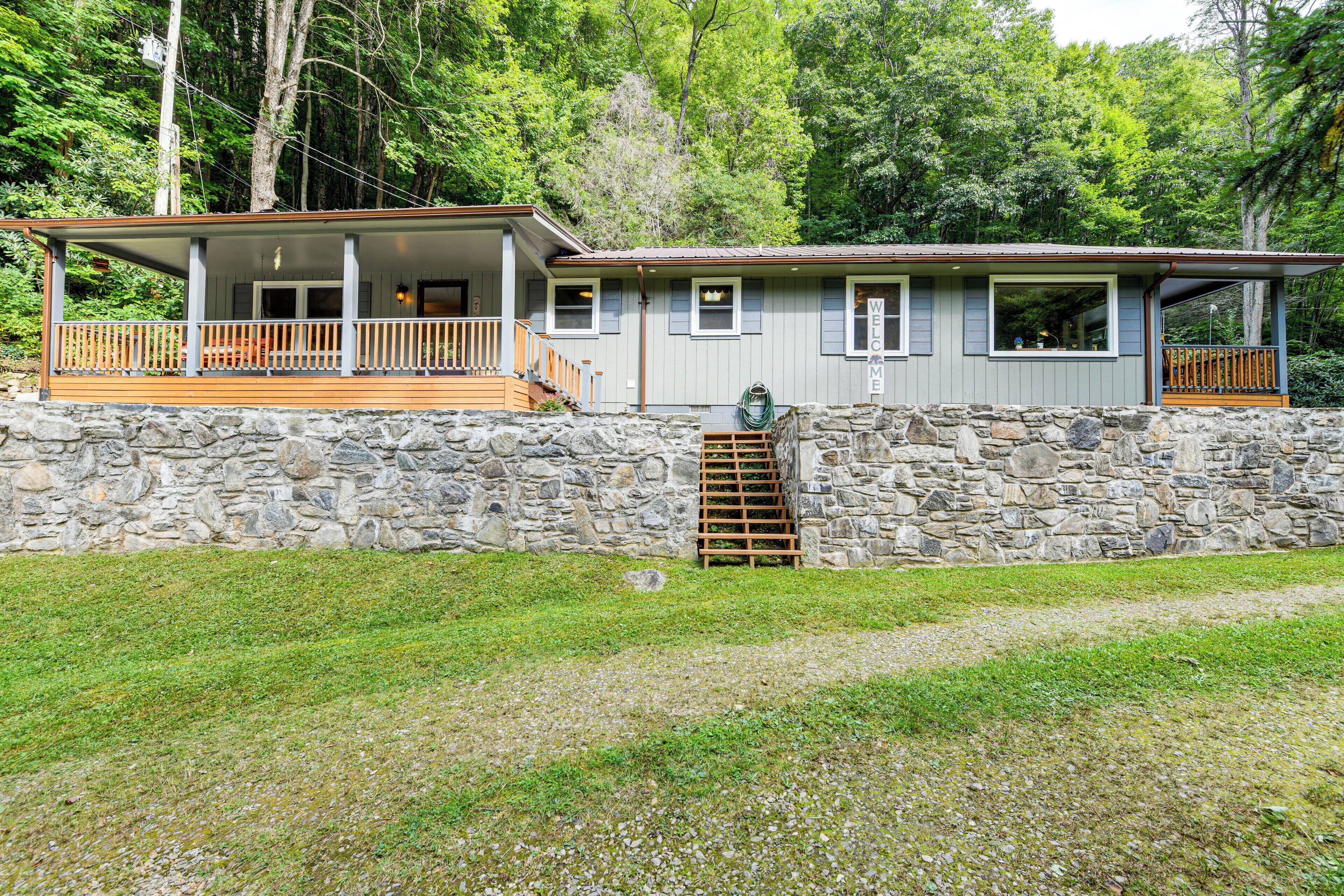 A two-story stone house with a wooden deck and a stone staircase leading to the upper level.