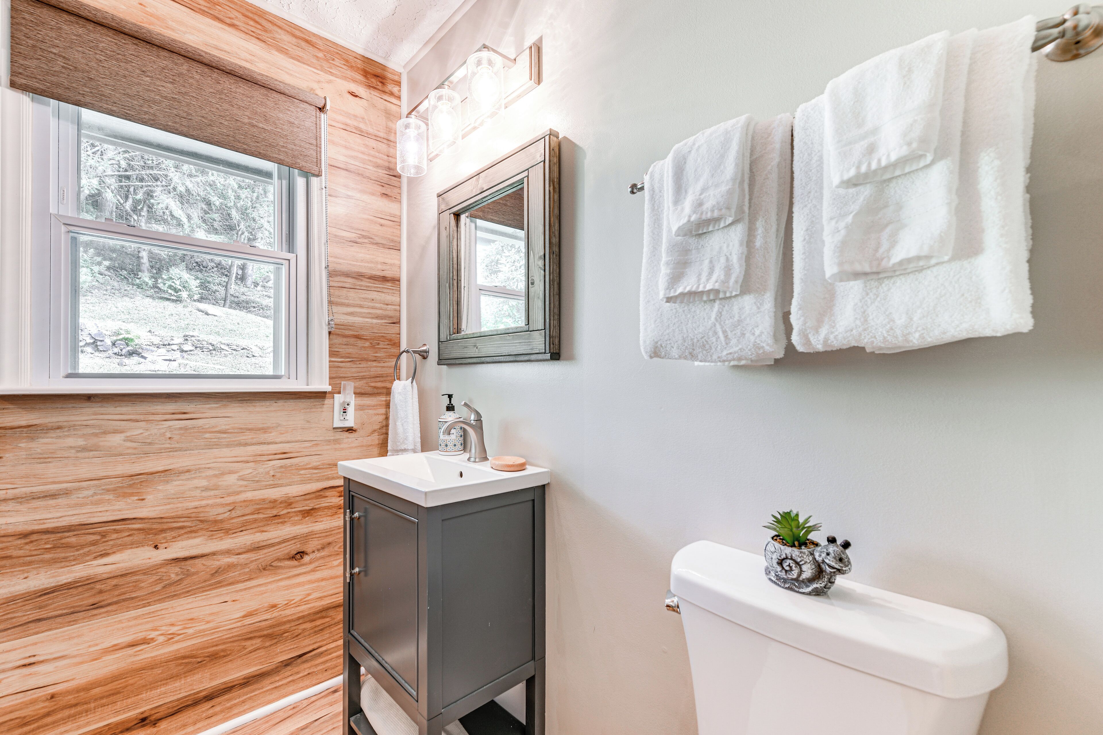 A bathroom with a wooden vanity, a white sink, a mirror, and a toilet.