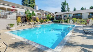 Una piscina con lettini e una piccola zona prendisole, circondata da un edificio con balconi e un giardino.