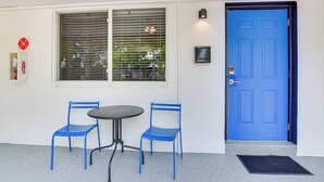 Una puerta azul, dos sillas azules, una mesa redonda y una ventana con persianas.