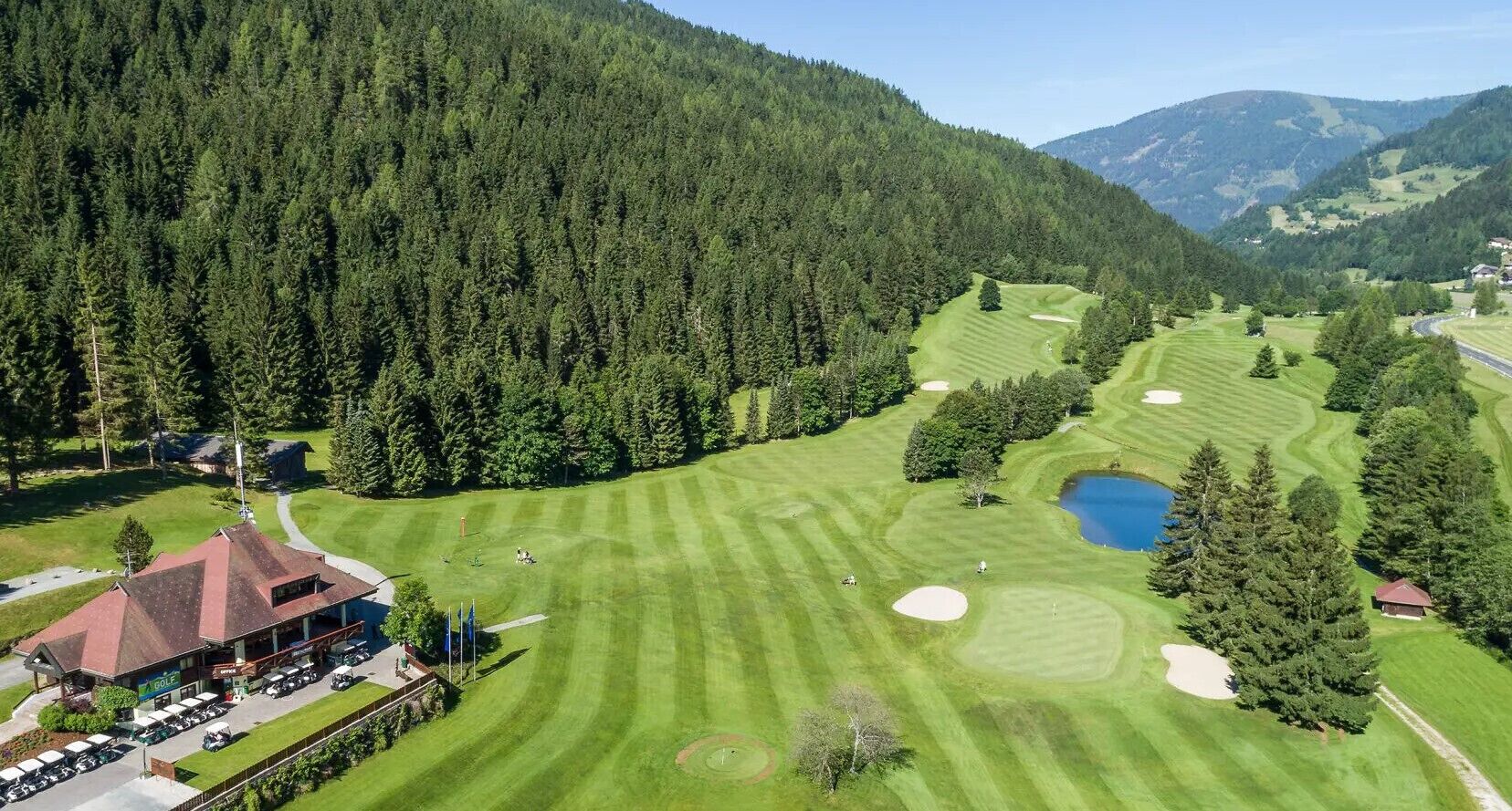 Vista aérea de um campo de golfe com um clube, rodeado por floresta densa e colinas.